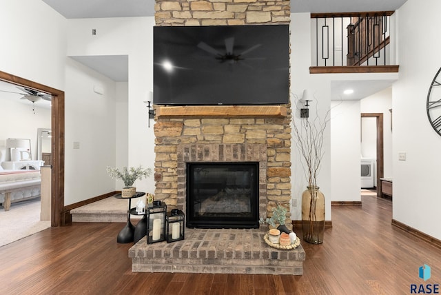 living room featuring wood-type flooring, washer / clothes dryer, a high ceiling, and a stone fireplace