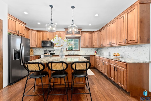 kitchen featuring sink, appliances with stainless steel finishes, dark hardwood / wood-style floors, a center island, and light stone countertops