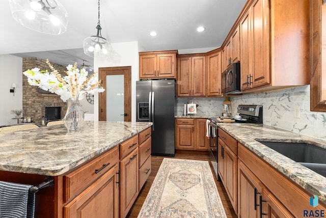 kitchen with a stone fireplace, appliances with stainless steel finishes, a center island, light wood-type flooring, and decorative backsplash