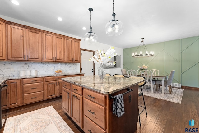 kitchen with a kitchen breakfast bar, light stone countertops, pendant lighting, a center island, and dark hardwood / wood-style floors