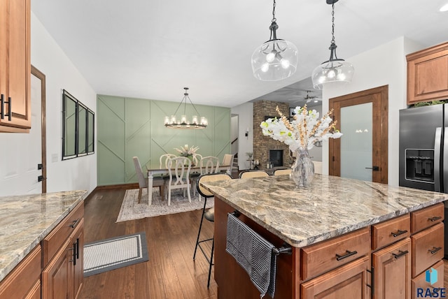 kitchen featuring dark hardwood / wood-style floors, stainless steel refrigerator with ice dispenser, a kitchen bar, a fireplace, and light stone countertops