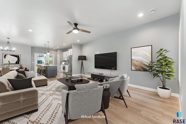 living room featuring ceiling fan with notable chandelier and light wood-type flooring