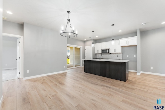 kitchen with an island with sink, white cabinets, light wood-type flooring, decorative light fixtures, and a notable chandelier