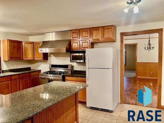 kitchen featuring decorative light fixtures, wall chimney exhaust hood, stainless steel appliances, dark stone countertops, and light hardwood / wood-style floors