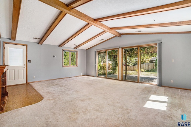 carpeted spare room featuring a textured ceiling, vaulted ceiling with beams, and plenty of natural light