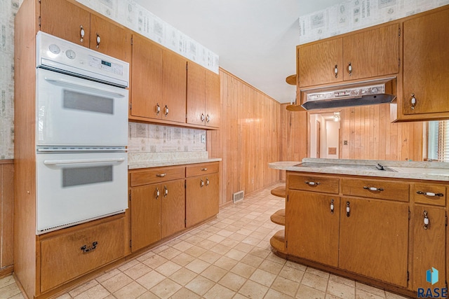 kitchen with white double oven, wooden walls, and stovetop