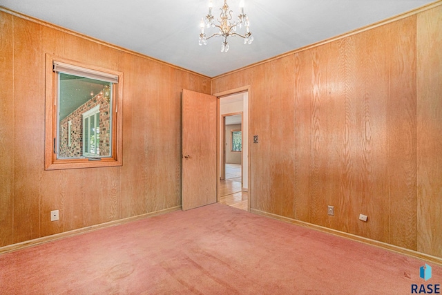 spare room featuring wood walls, light colored carpet, and a notable chandelier