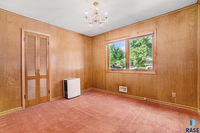 empty room featuring a notable chandelier, wooden walls, and carpet