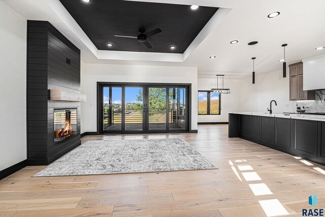 313 Red Spruce Ave, Sioux Falls, SD 57110 - unfurnished living room featuring baseboards, a raised ceiling, a multi sided fireplace, ceiling fan, and light wood-style floors