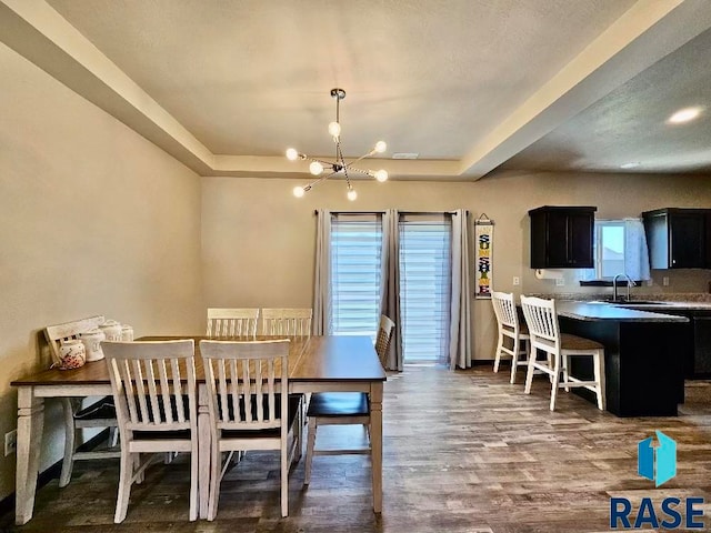 dining room featuring sink, a chandelier, wood-type flooring, and a tray ceiling