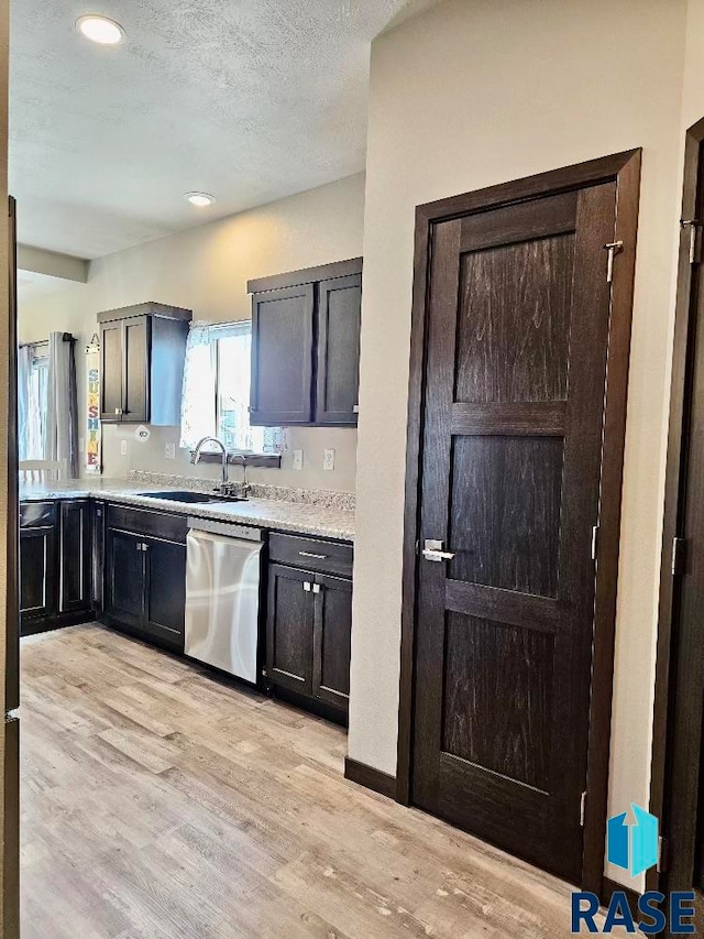 kitchen with light stone countertops, sink, a textured ceiling, stainless steel dishwasher, and light hardwood / wood-style flooring