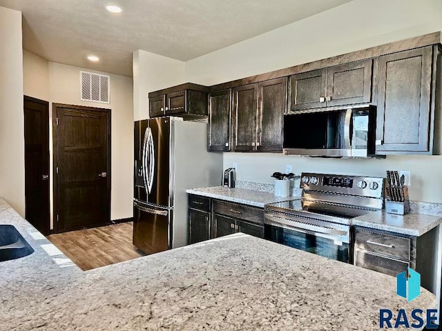 kitchen with appliances with stainless steel finishes, light stone counters, dark brown cabinets, and light hardwood / wood-style floors