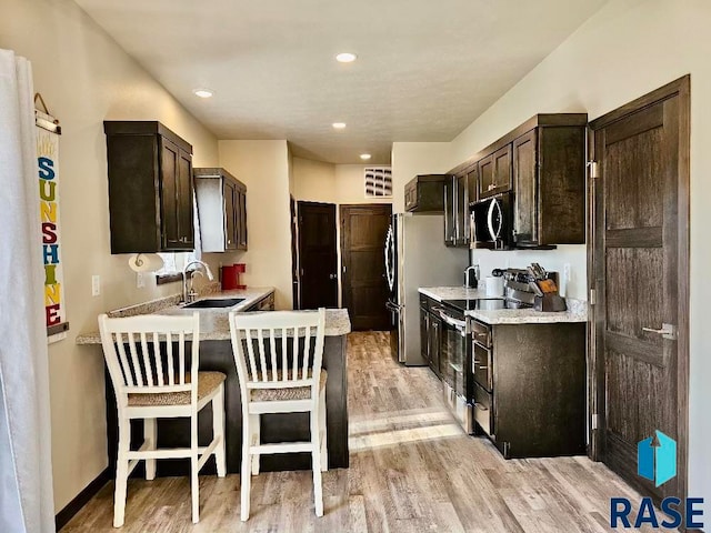 kitchen featuring dark brown cabinets, a kitchen breakfast bar, light wood-type flooring, sink, and stainless steel appliances