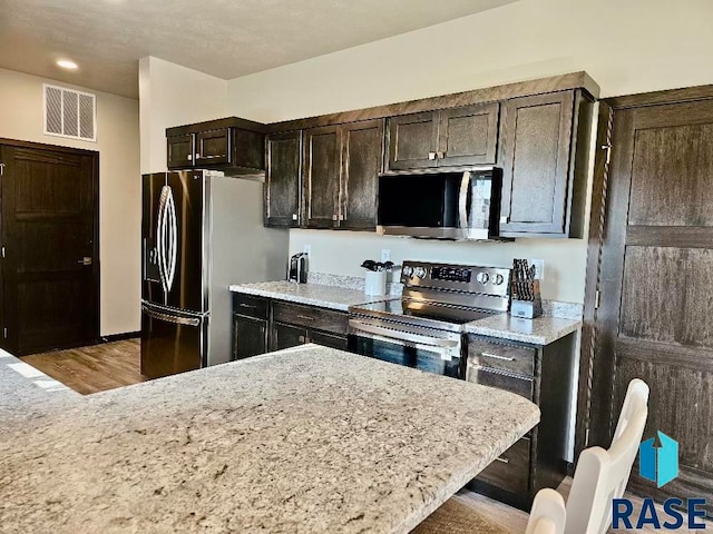 kitchen featuring appliances with stainless steel finishes, hardwood / wood-style floors, light stone countertops, and dark brown cabinets