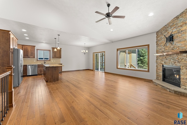 unfurnished living room featuring ceiling fan with notable chandelier, a stone fireplace, sink, and light hardwood / wood-style flooring