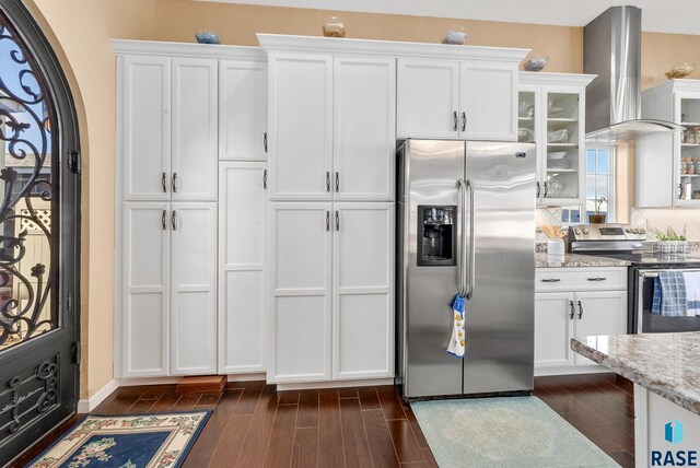 kitchen featuring white cabinets, light stone counters, appliances with stainless steel finishes, and wall chimney range hood