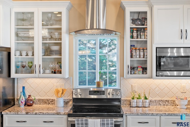 kitchen with wall chimney exhaust hood, stainless steel appliances, white cabinets, and backsplash