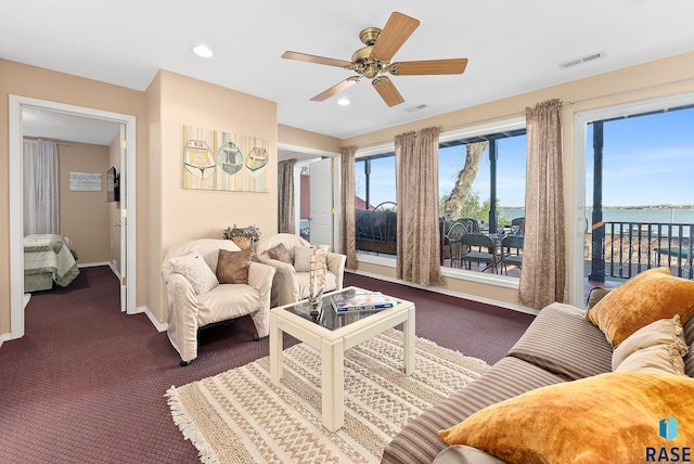 carpeted living room with a water view and ceiling fan