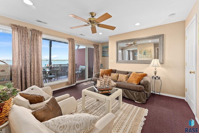 carpeted living room featuring ceiling fan and a water view