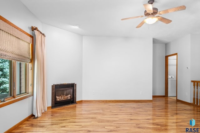 unfurnished living room featuring washer / dryer, a glass covered fireplace, light wood-style flooring, and baseboards