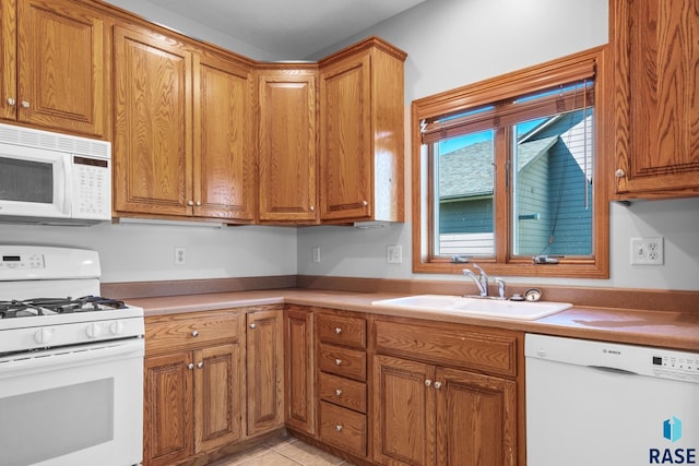 kitchen featuring brown cabinets, light countertops, light tile patterned flooring, a sink, and white appliances