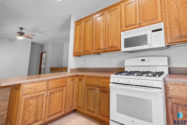 kitchen with light tile patterned floors, brown cabinetry, ceiling fan, white appliances, and a peninsula