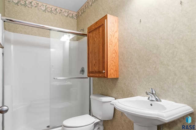 bathroom featuring a stall shower, a sink, toilet, and wallpapered walls