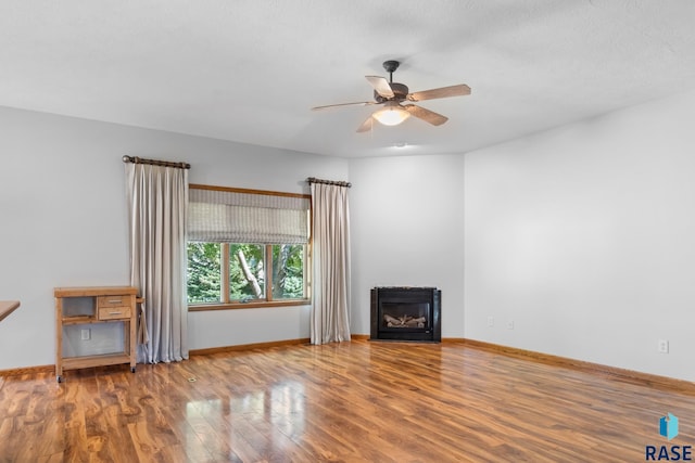 unfurnished living room featuring a fireplace, wood finished floors, a ceiling fan, and baseboards