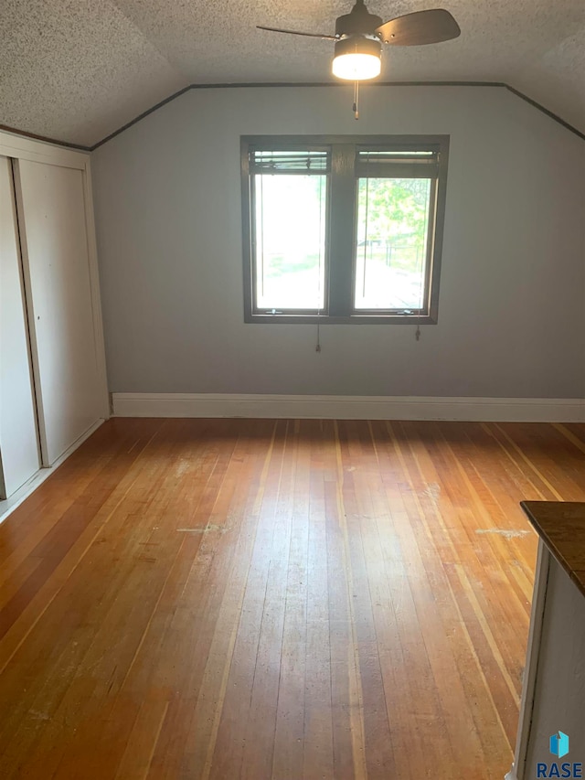 additional living space with wood-type flooring, a textured ceiling, vaulted ceiling, and ceiling fan