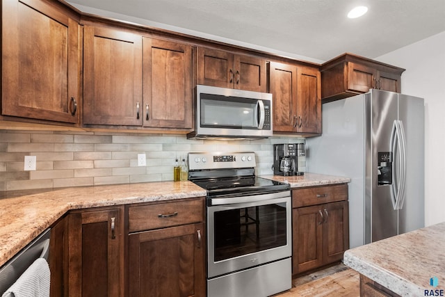 kitchen featuring decorative backsplash, light hardwood / wood-style floors, appliances with stainless steel finishes, and light stone counters