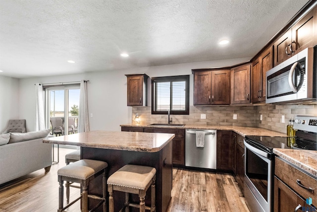 kitchen with a center island, appliances with stainless steel finishes, a kitchen bar, and light wood-type flooring