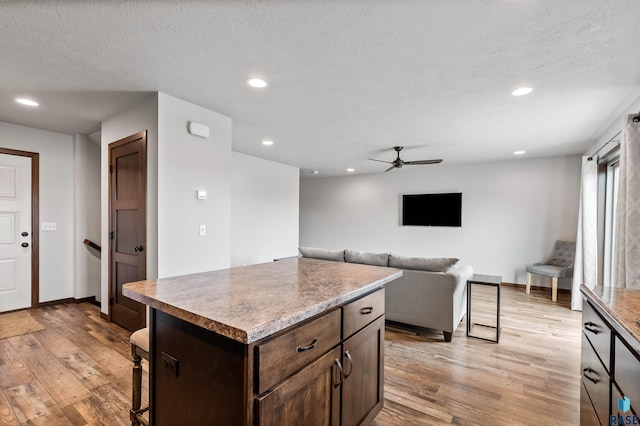 kitchen with ceiling fan, a textured ceiling, light hardwood / wood-style floors, and a kitchen island