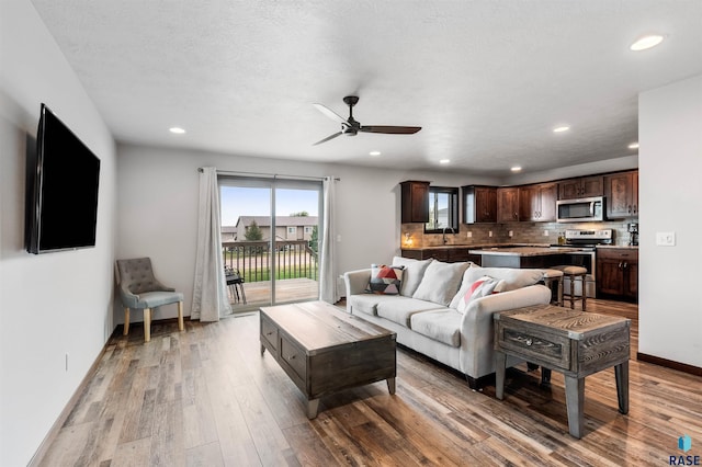 living room with ceiling fan, a textured ceiling, light hardwood / wood-style flooring, and sink