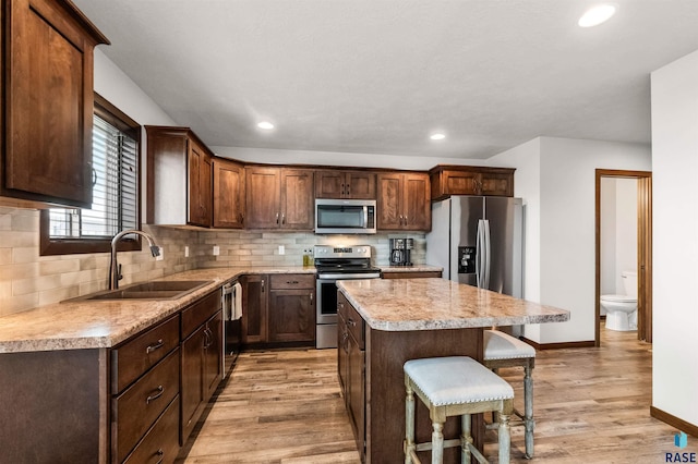 kitchen with appliances with stainless steel finishes, sink, a center island, and light hardwood / wood-style flooring