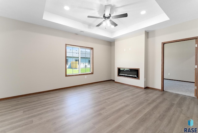 unfurnished living room featuring ceiling fan, a raised ceiling, and light wood-type flooring