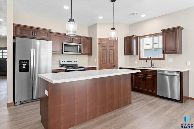 kitchen with sink, decorative light fixtures, appliances with stainless steel finishes, a center island, and light hardwood / wood-style floors