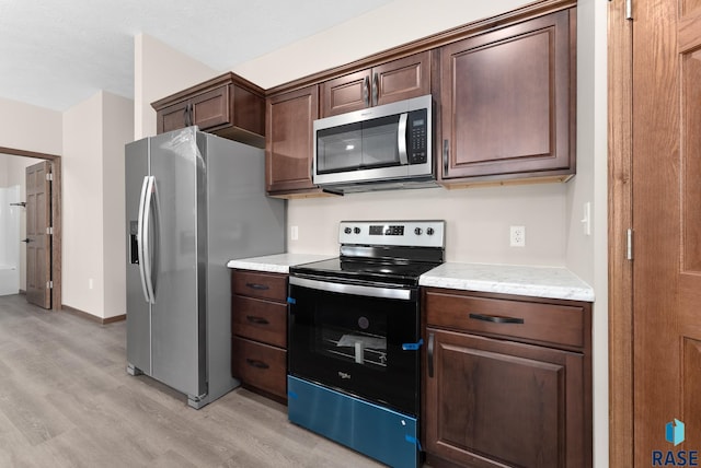 kitchen with dark brown cabinetry, light stone countertops, stainless steel appliances, and light hardwood / wood-style flooring