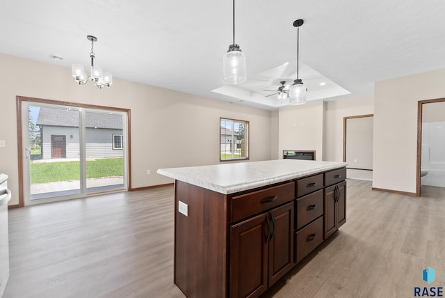 kitchen featuring hanging light fixtures, a tray ceiling, a kitchen island, and light hardwood / wood-style flooring