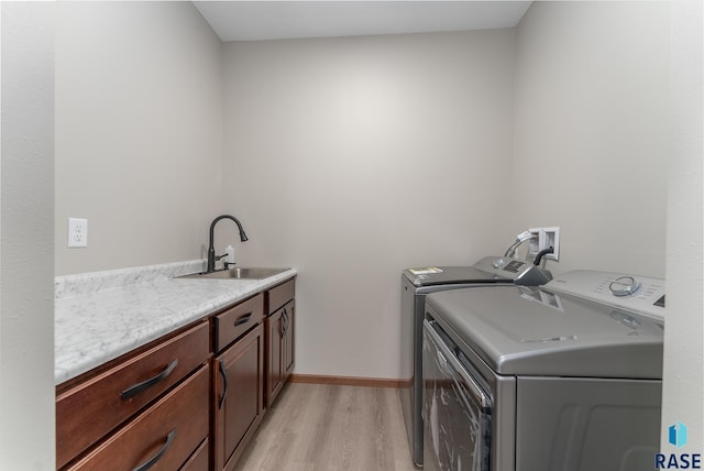 laundry room with light wood-type flooring, washer and clothes dryer, sink, and cabinets