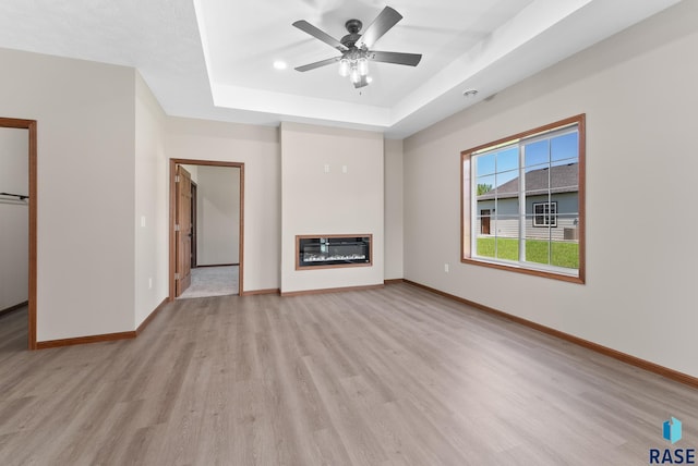 unfurnished living room with a raised ceiling, ceiling fan, and light hardwood / wood-style flooring