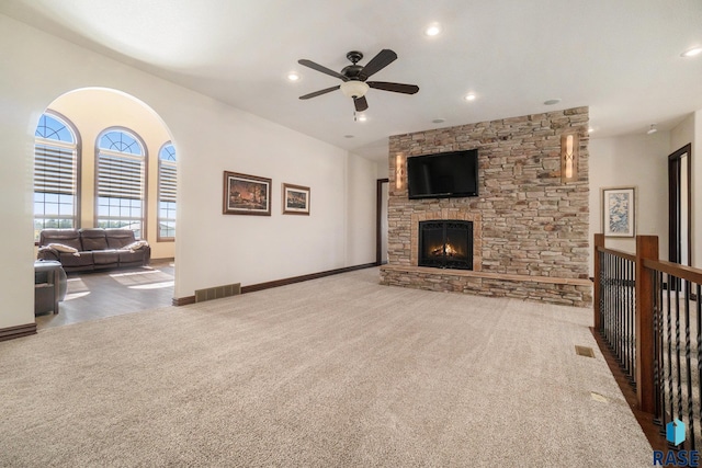 carpeted living room featuring ceiling fan and a stone fireplace