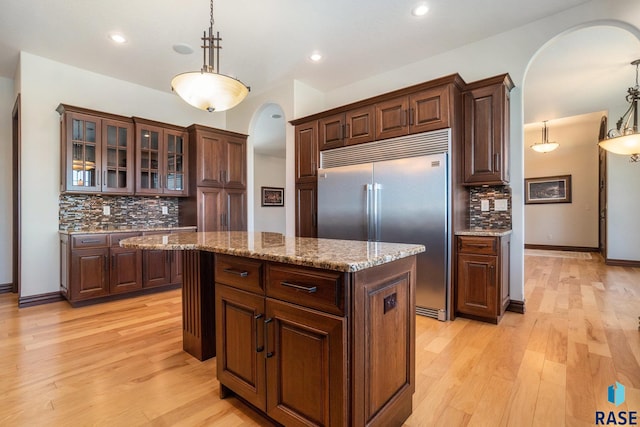 kitchen featuring stainless steel built in fridge, a kitchen island, decorative light fixtures, light wood-type flooring, and decorative backsplash