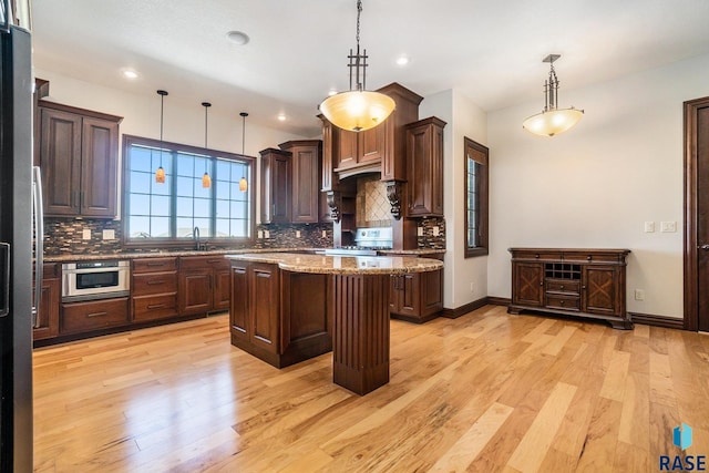 kitchen with light stone counters, pendant lighting, light hardwood / wood-style floors, and a center island