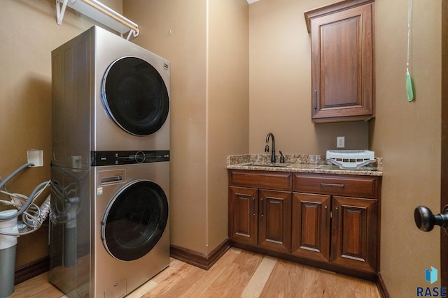 clothes washing area featuring cabinets, sink, light hardwood / wood-style floors, and stacked washer / drying machine