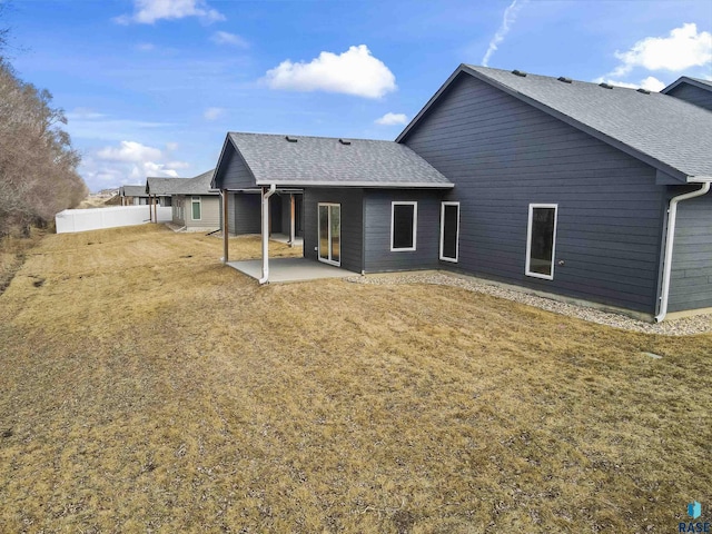 rear view of property with a patio area, roof with shingles, fence, and a lawn