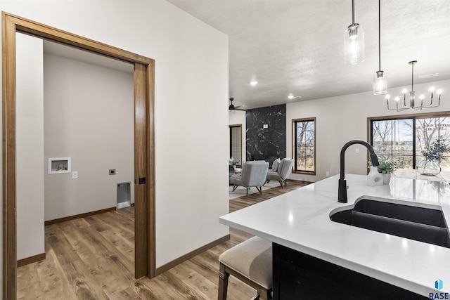 kitchen with light wood finished floors, baseboards, light countertops, pendant lighting, and a sink