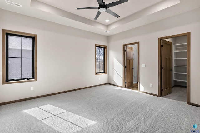 unfurnished bedroom featuring light carpet, visible vents, baseboards, a tray ceiling, and a walk in closet