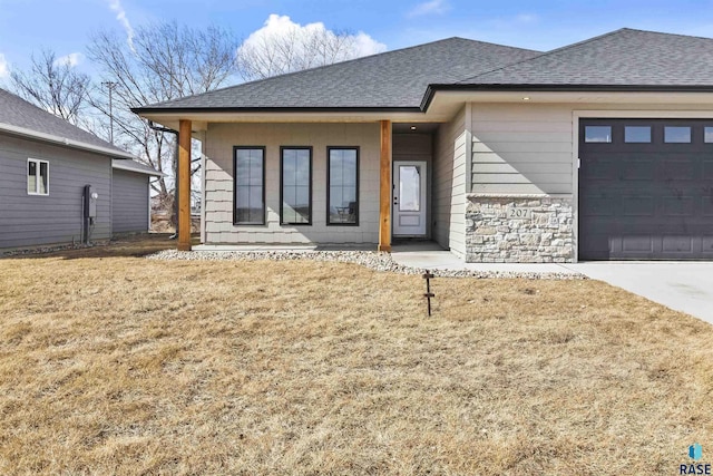 view of front facade featuring a garage, driveway, stone siding, roof with shingles, and a front yard