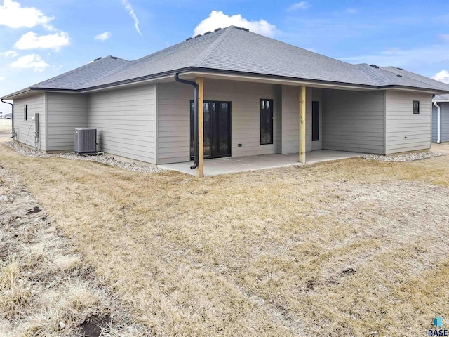 rear view of house featuring a shingled roof, a lawn, central AC, and a patio