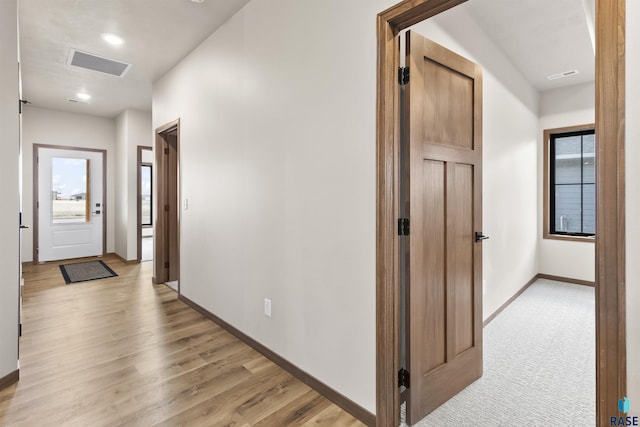 hall with visible vents, baseboards, light wood-style flooring, and a wealth of natural light